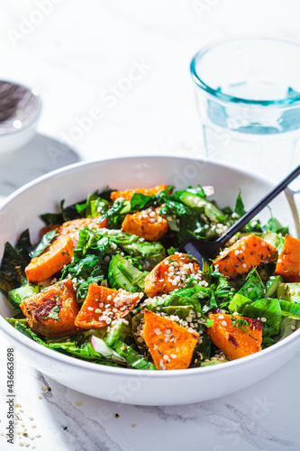 Baked sweet potato with green salad in a white bowl. Vegan food concept.