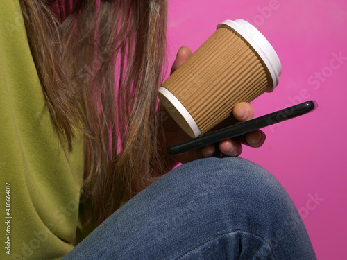 Woman using mobile phone with coffee on magenta background photo