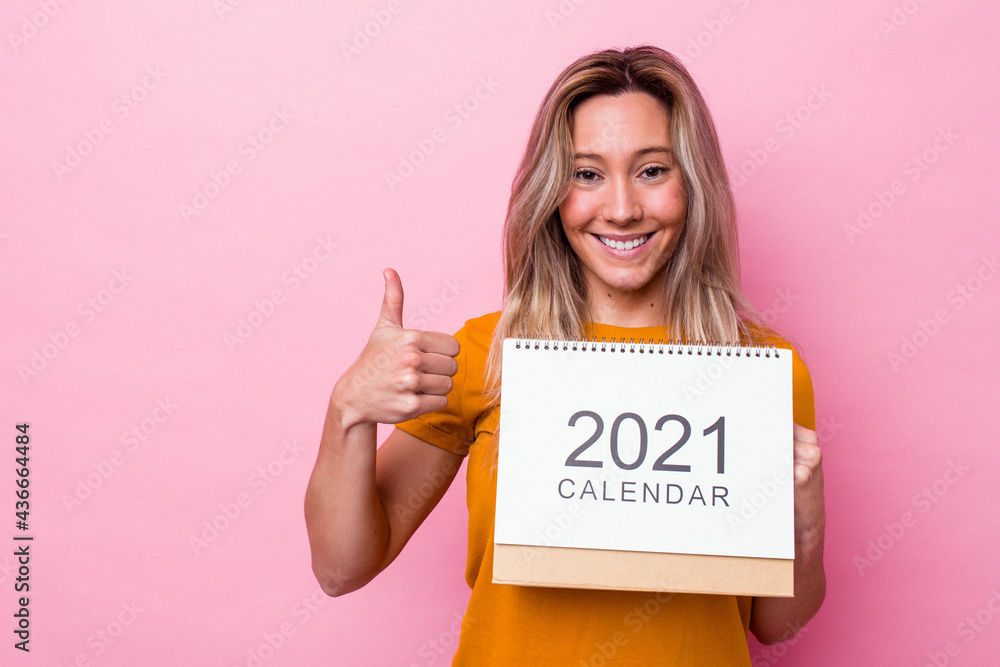 Young australian woman holding a calendar isolated on pink background smiling and raising thumb up Young australian woman holding a calendar isolated on pink background smiling and raising thumb up