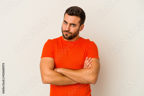 Young caucasian man isolated on white background frowning face in displeasure, keeps arms folded.