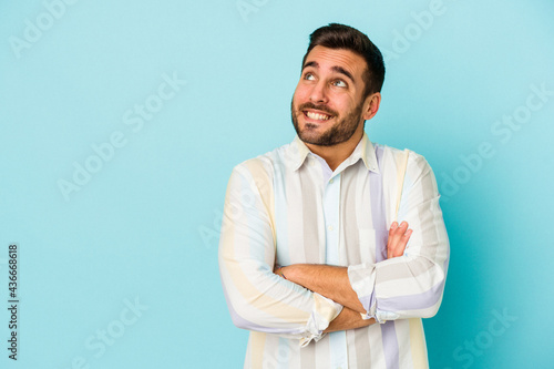 Young caucasian man isolated on blue background smiling confident with crossed arms.