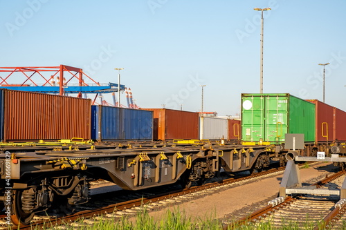 Railway freight waggons with containers on tracks in the harbour on a sunny day with blue sky and container bridges in the background