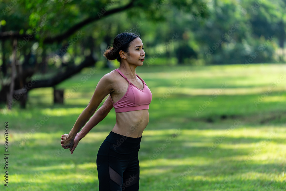 Asian woman wearing sportwear warming up stretch her arms and body in public park Asian woman wearing sportwear warming up stretch her arms and body in public park