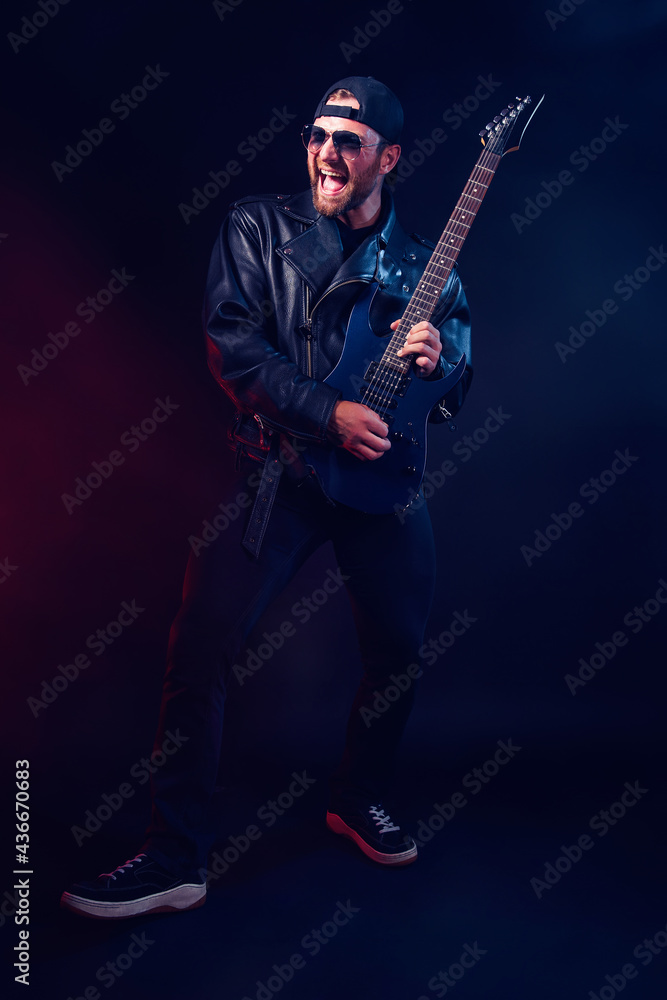 Full size photo of brutal bearded Heavy metal musician in leather jacket and sunglasses is playing electrical guitar very emotionally. Shot in a studio on dark background Full size photo of brutal bearded Heavy metal musician in leather jacket and sunglasses is playing electrical guitar very emotionally. Shot in a studio on dark background