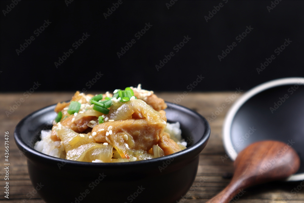 rice stir korean sauce with chicken in black ceramic bowl is served on the wooden table runner with wooden spoon with black wall background during dinner in the Japanese restaurant rice stir korean sauce with chicken in black ceramic bowl is served on the wooden table runner with wooden spoon with black wall background during dinner in the Japanese restaurant