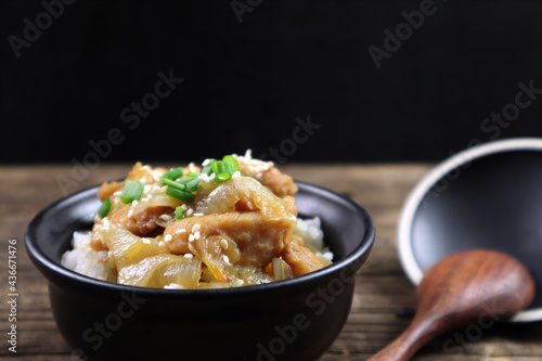 rice stir korean sauce with chicken in black ceramic bowl is served on the wooden table runner with wooden spoon with black wall background during dinner in the Japanese restaurant