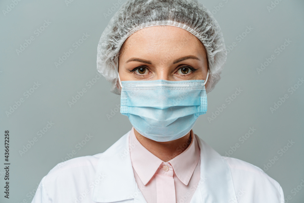 Portrait of an unhappy young woman doctor in a medical mask on a gray background. The doctor's tired eyes. The concept of coronavirus. Portrait of an unhappy young woman doctor in a medical mask on a gray background. The doctor's tired eyes. The concept of coronavirus.