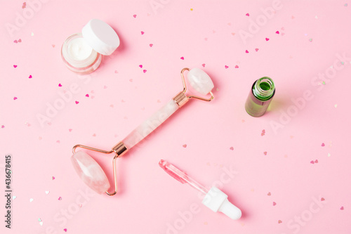 Massage quartz roller and dropper with cosmetic product on pink background