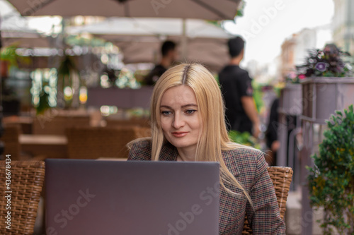 young blonde woman sitting with laptop on summer terrace and smiling. front view © Mikhail