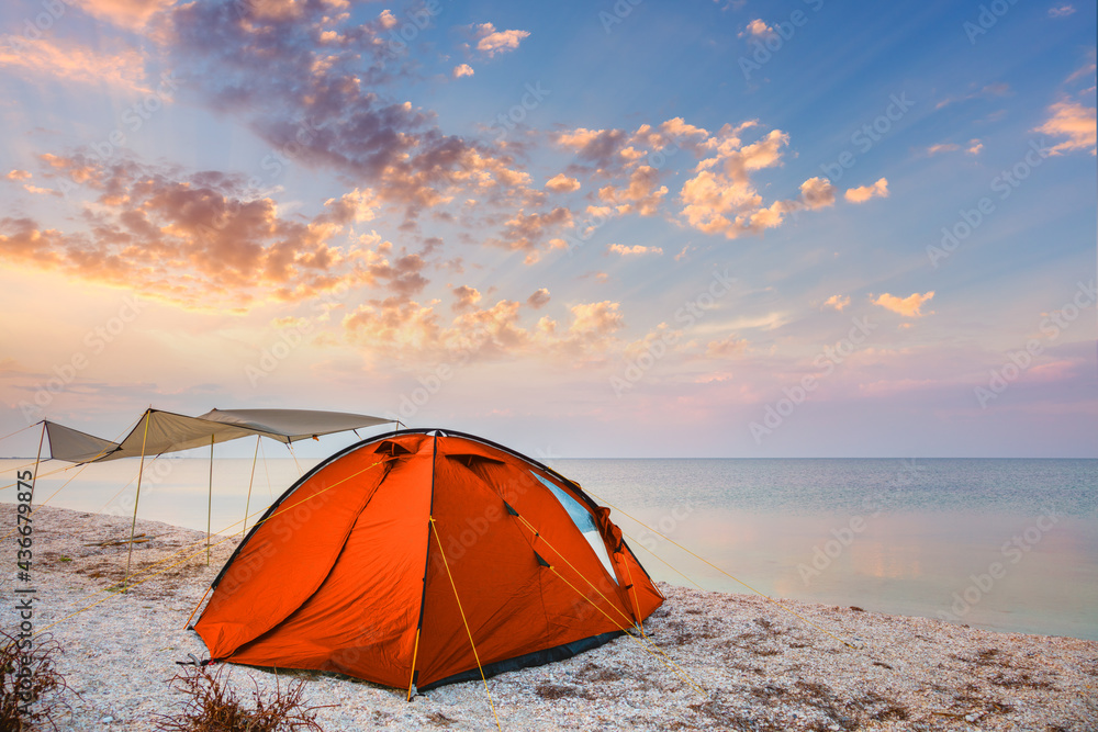 Camp tent on a beautiful quiet beach near the water against  the sunset sky background
