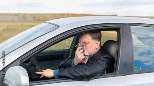 A sick driver wipes his nose with a handkerchief at the wheel of a car on way to the hospital.