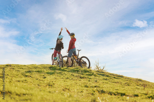 Fototapeta Naklejka Na Ścianę i Meble -  Two happy woman high five over the sunset after a successful mountain biking trip in the mountains. Celebrate a cross country cycling journey.