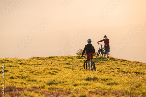 Mother waiting for daughter cycling downhill with mountain bike at a sunset.