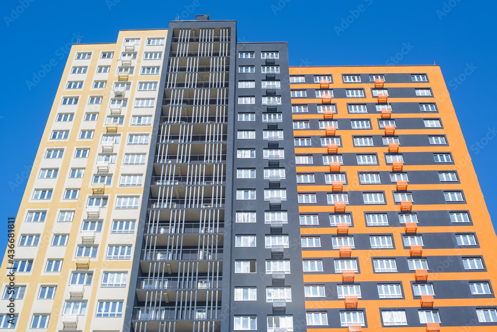 Multi-storey residential building outside. Tenement building, bottom-up view. Multicolored modern building against the blue sky during the day.