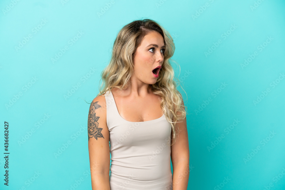 Young Brazilian woman isolated on blue background doing surprise gesture while looking to the side Young Brazilian woman isolated on blue background doing surprise gesture while looking to the side
