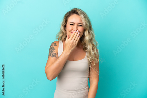 Young Brazilian woman isolated on blue background happy and smiling covering mouth with hand