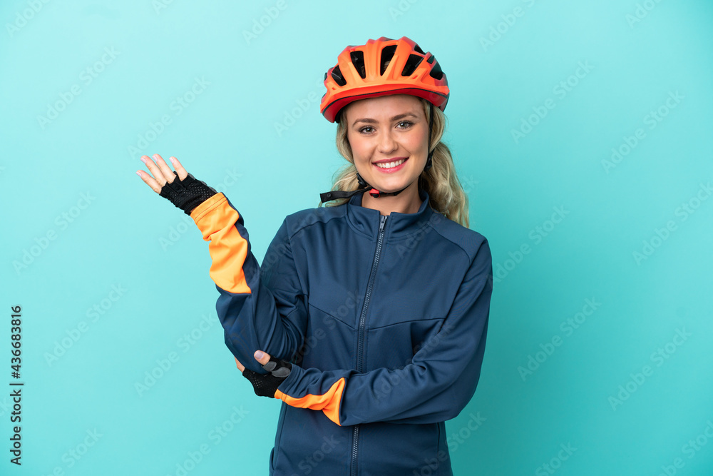 Young cyclist woman isolated on blue background extending hands to the side for inviting to come Young cyclist woman isolated on blue background extending hands to the side for inviting to come