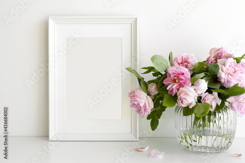Fototapeta Naklejka Na Ścianę i Meble -  Indoor image of pinkish peony flowers arranged in vase on table with vertical rectangular photo frame with copy space for your picture or design. Home, decoration, interior and memory concept