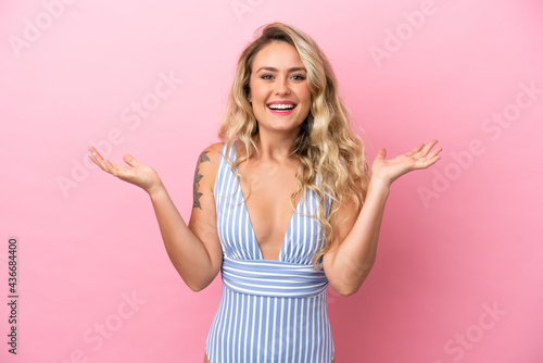 Young Brazilian woman in swimsuit in summer holidays isolated on pink background with shocked facial expression