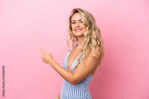 Young Brazilian woman in swimsuit in summer holidays isolated on pink background pointing back