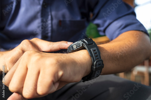 businessman wearing digital smart watch in hand touching screen to open notification, read message and activity tracker in wrist with soft-focus and over light in the background.