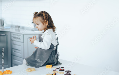 Little girl cooking sweet cookies, sitting on table