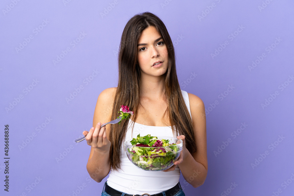 Teenager Brazilian girl holding a salad over isolated purple background Teenager Brazilian girl holding a salad over isolated purple background