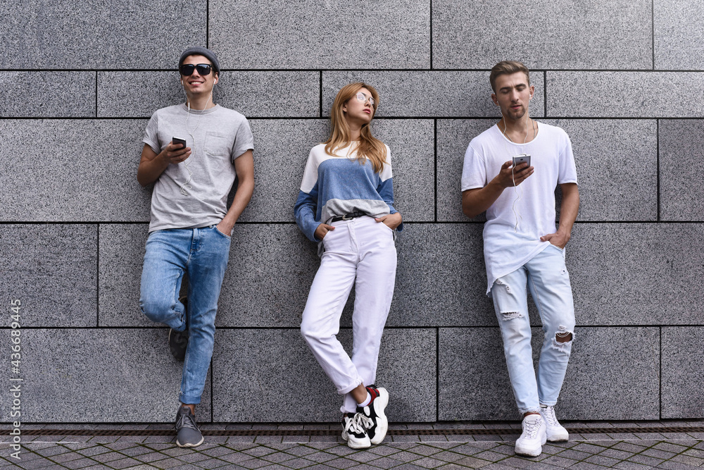 Fototapeta premium Fashion portrait of Three best friends posing at street, wearing stylish outfit and jeans against gray wall .