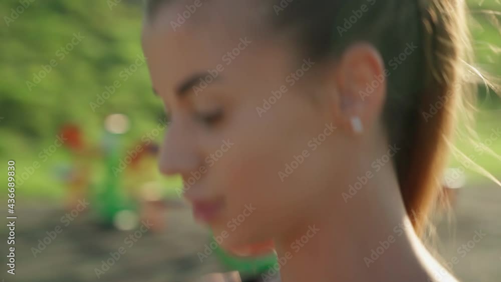 Close up motion of young athlete woman wearing sports bra and shorts running outdoors. Girl with long chestnut pony tail practicing jogging at stadium in sunny summer day. Sport concept. Close up motion of young athlete woman wearing sports bra and shorts running outdoors. Girl with long chestnut pony tail practicing jogging at stadium in sunny summer day. Sport concept.
