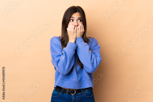 Teenager Brazilian girl over isolated background nervous and scared putting hands to mouth