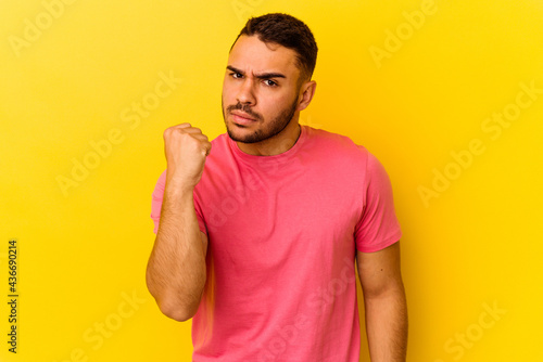 Young caucasian man isolated on yellow background showing fist to camera, aggressive facial expression.