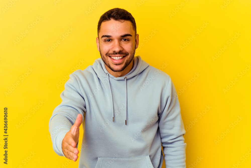 Young caucasian man isolated on yellow background stretching hand at camera in greeting gesture. Young caucasian man isolated on yellow background stretching hand at camera in greeting gesture.