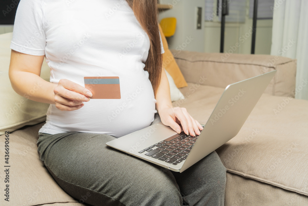 Naklejka premium Online shopping on the Internet. Pregnant girl at the computer, pays for children's shopping with a card