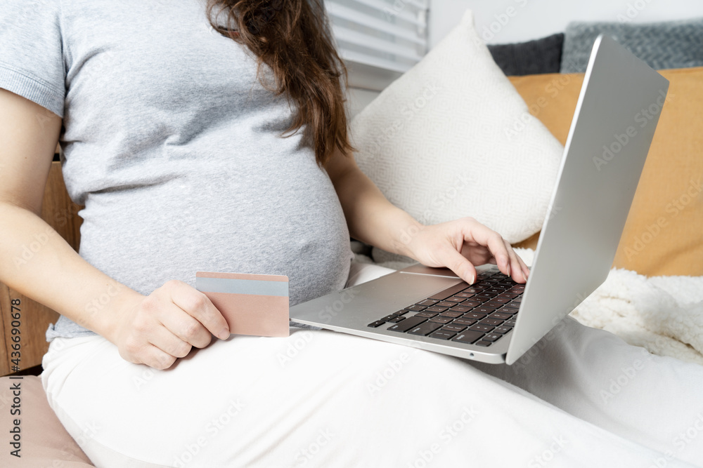 Fototapeta premium Online shopping on the Internet. Pregnant girl at the computer, pays for children's shopping with a card