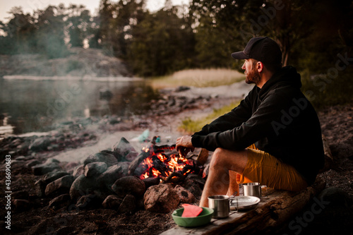 Side view of mature man sitting by campfire while looking away during sunset photo