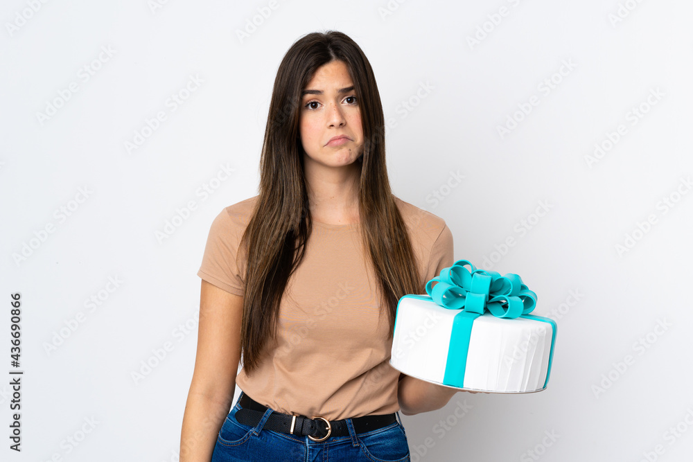 Teenager pastry chef holding a big cake over isolated white background with sad expression Teenager pastry chef holding a big cake over isolated white background with sad expression