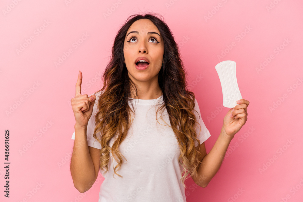 Young mexican woman holding a compress isolated on pink background pointing upside with opened mouth. Young mexican woman holding a compress isolated on pink background pointing upside with opened mouth.