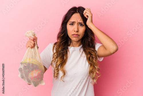 Foto Young mexican woman holding a fruit bag isolated on pink background being shocked, she has remembered important meeting