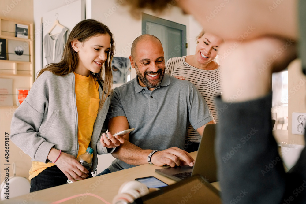 Smiling woman and daughter looking at man doing online shopping at home