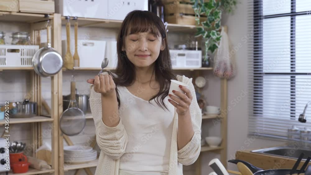 happy asian young woman is licking the spoon with a contented smile while enjoying a cup of delicious yogurt in the morning at home. happy asian young woman is licking the spoon with a contented smile while enjoying a cup of delicious yogurt in the morning at home.