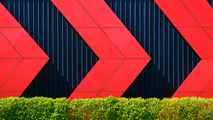 Front view of red arrows pattern on black corrugated metal wall behind green bush fence in exterior architecture decorations design concept