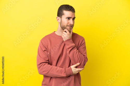 Handsome blonde man over isolated yellow background having doubts and thinking
