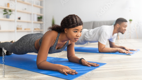 Young black couple standing in elbow plank on yoga mats, doing domestic fitness, exercising their muscles indoors