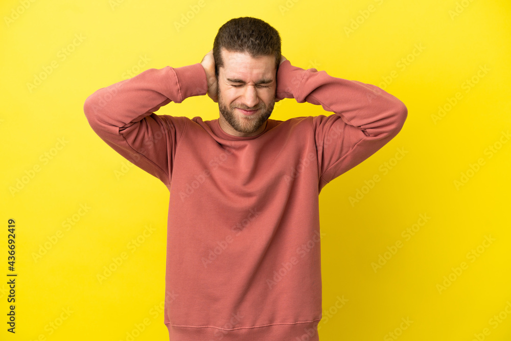 Handsome blonde man over isolated yellow background frustrated and covering ears Handsome blonde man over isolated yellow background frustrated and covering ears