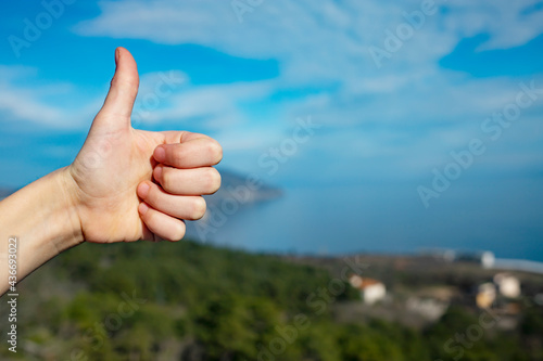 Thumb up on a background of blue sky and nature on a summer sunny day.