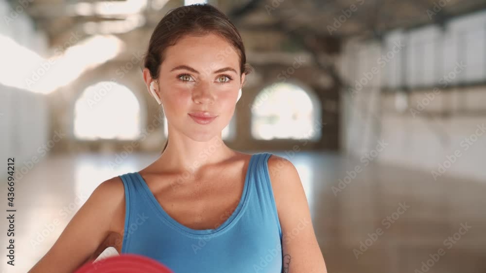 A smiling woman wearing a blue sports suit is holding a yoga mat in sport gym A smiling woman wearing a blue sports suit is holding a yoga mat in sport gym