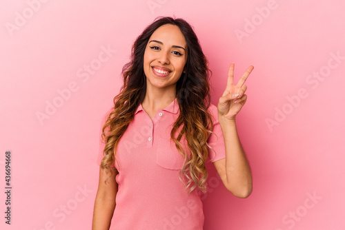 Young mexican woman isolated on pink background joyful and carefree showing a peace symbol with fingers. © Asier