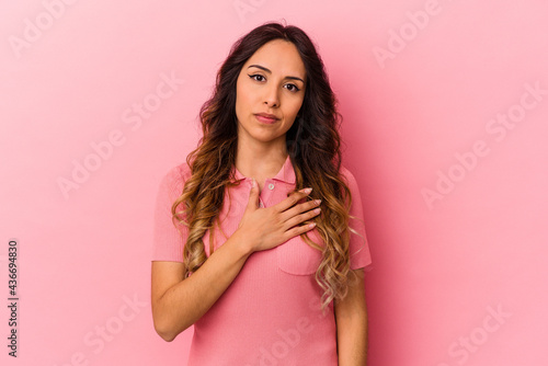 Young mexican woman isolated on pink background taking an oath  putting hand on chest.
