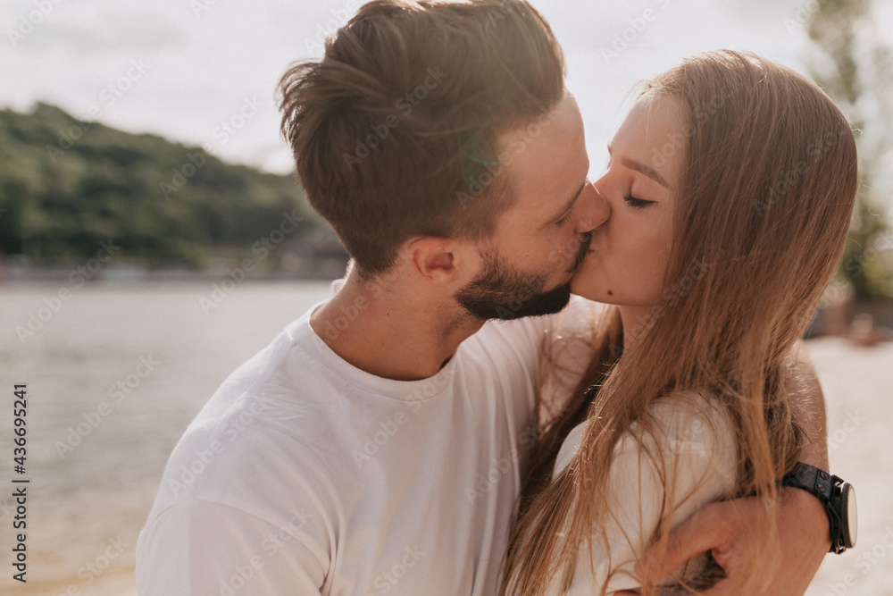 Close-up portrait of kissing young people outside in sunny warm day. Handsome brunette man is hugging and kissing her girlfriend while spend time outdoor Close-up portrait of kissing young people outside in sunny warm day. Handsome brunette man is hugging and kissing her girlfriend while spend time outdoor