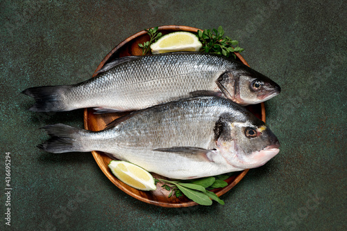 Uncooked fish with lime and herbs in a wooden bowl on a dark green background top view. Raw dorada and seabass. photo